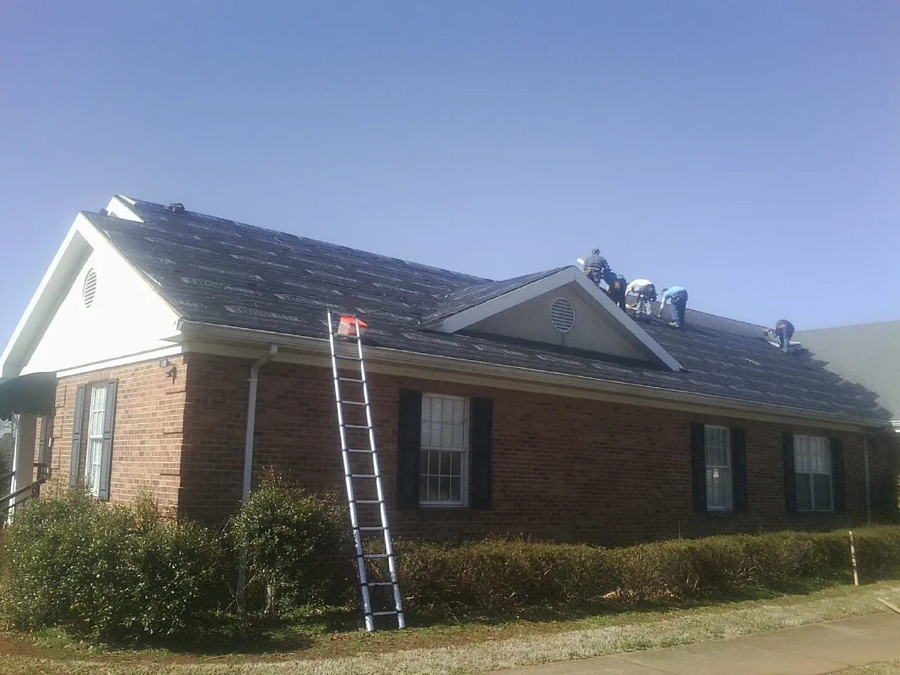 Crew tearing shingles off a brick ranch roof with a ladder set — Emergency Roof Repair work by our crew in Exeter