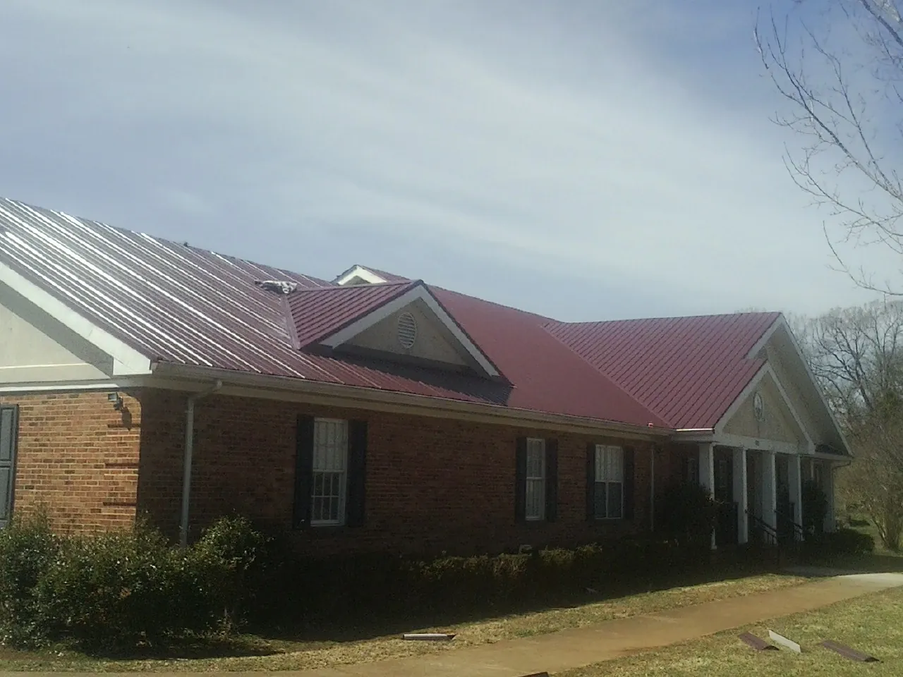 Red metal roof with gabled entries on a long brick building, from a Hail Damage Roof Repair job in Exeter